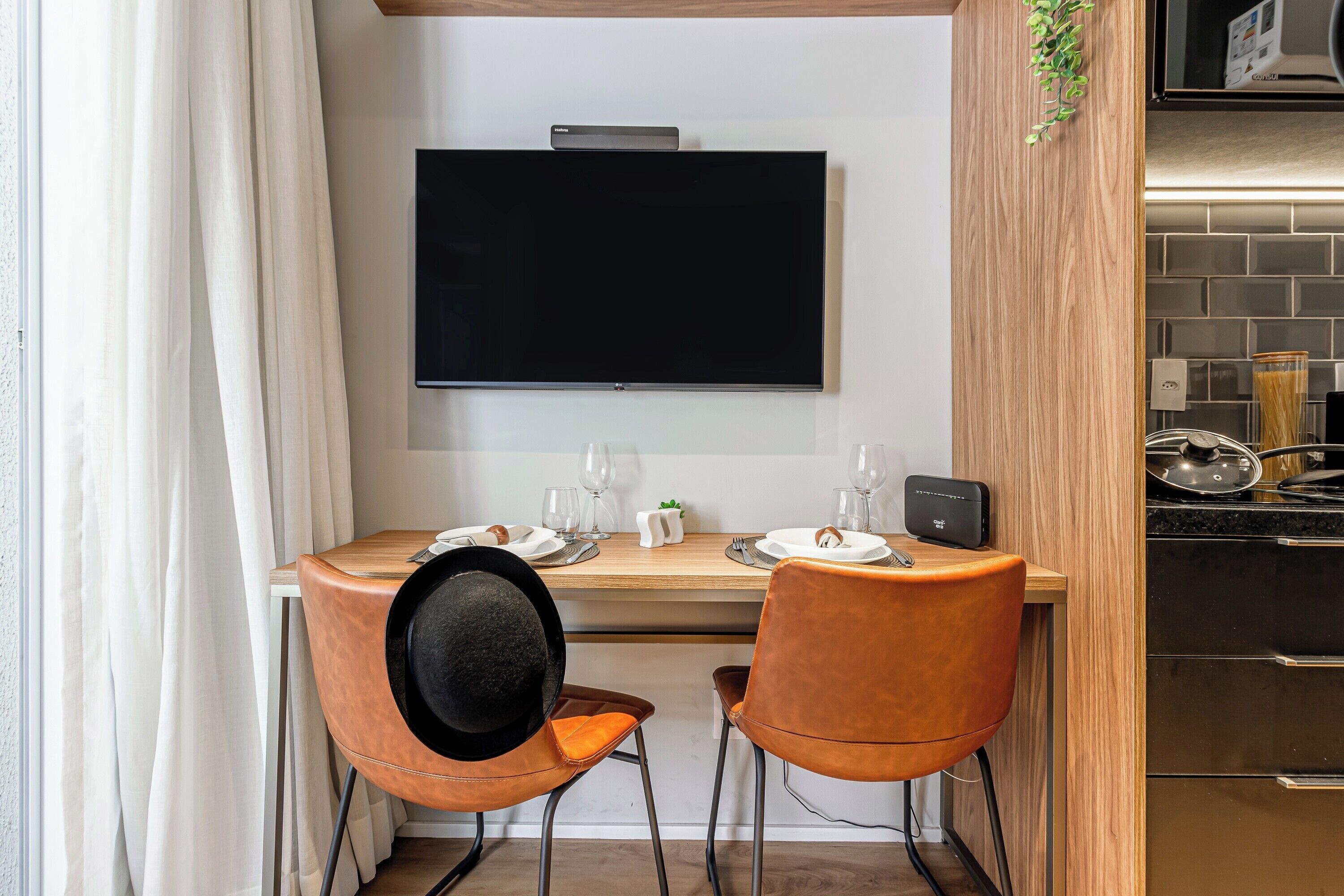 A compact kitchen with a flat-screen TV, two chairs, a dining table set for two, and a modern stove.