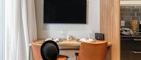 A compact kitchen with a flat-screen TV, two chairs, a dining table set for two, and a modern stove.