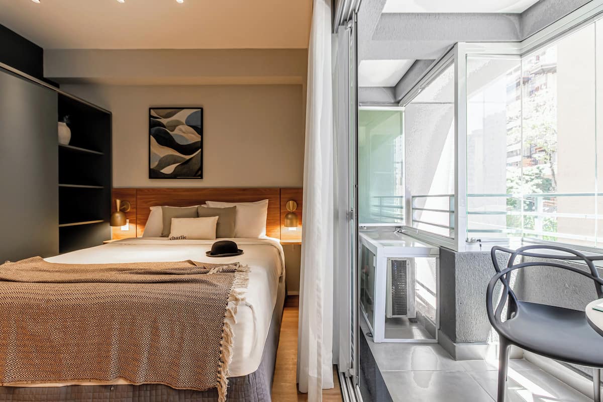 A bedroom with a bed, bedside tables, a wardrobe, a painting, and a balcony with a chair.