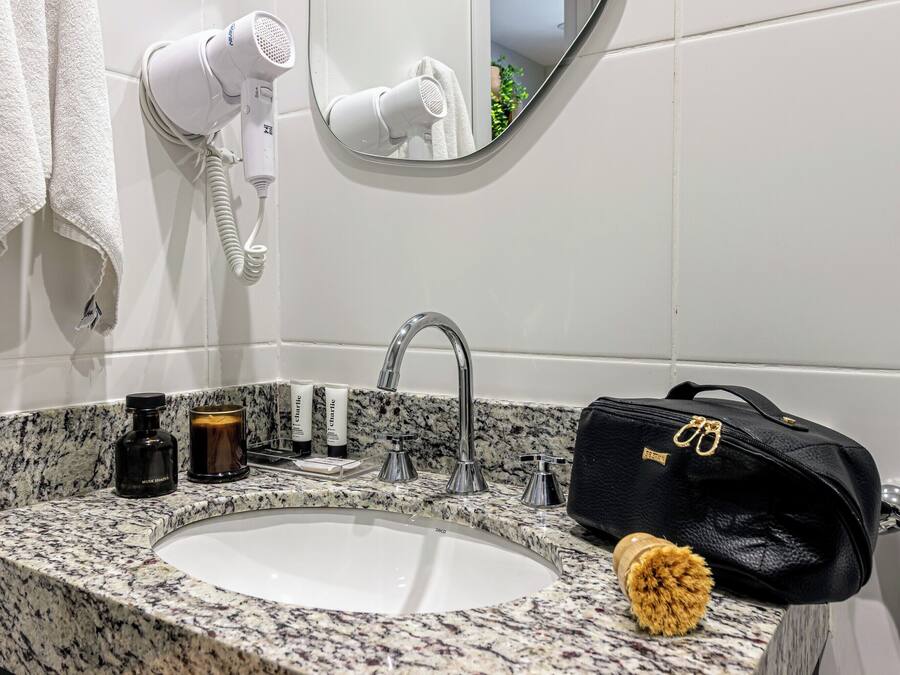Un baño con lavamanos, espejo, secador de pelo, toalla, artículos de aseo personal y una bolsa.