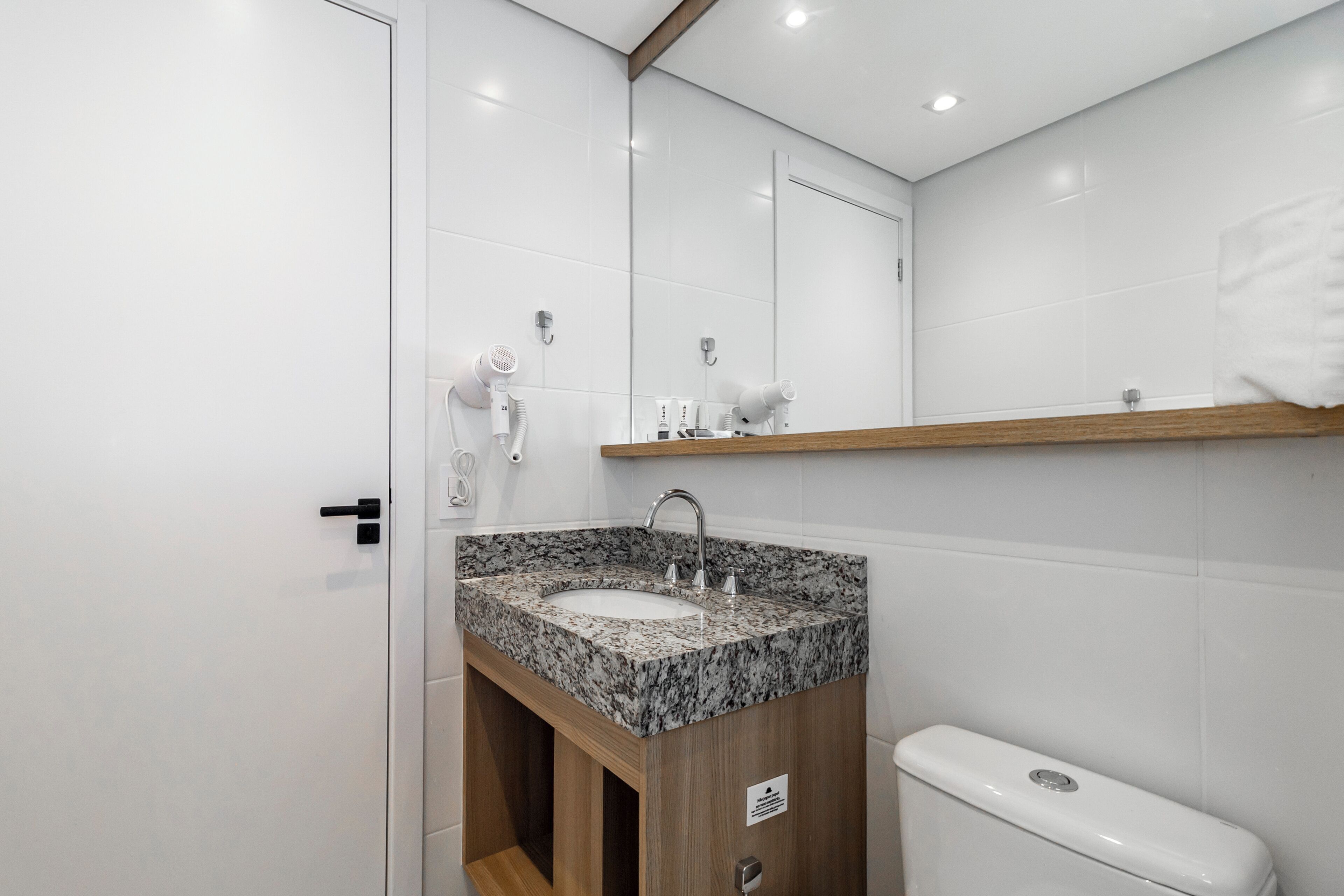 Ein modernes Badezimmer mit einem Granitwaschbecken, einem Holzschrank, einer weißen Toilette und einem Spiegel über dem Waschbecken.