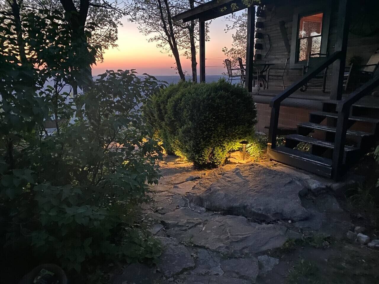 Un espace extérieur rustique agrémenté d’un chemin de pierre, d’une pergola en bois et offrant une vue sur le coucher de soleil.