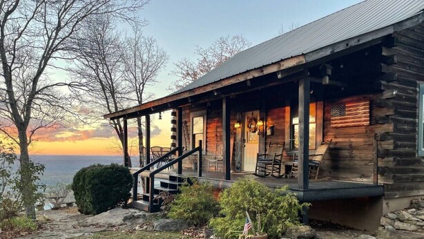 Een vakantiehuis in blokhutstijl met een veranda, buitenmeubels en uitzicht op het landschap.