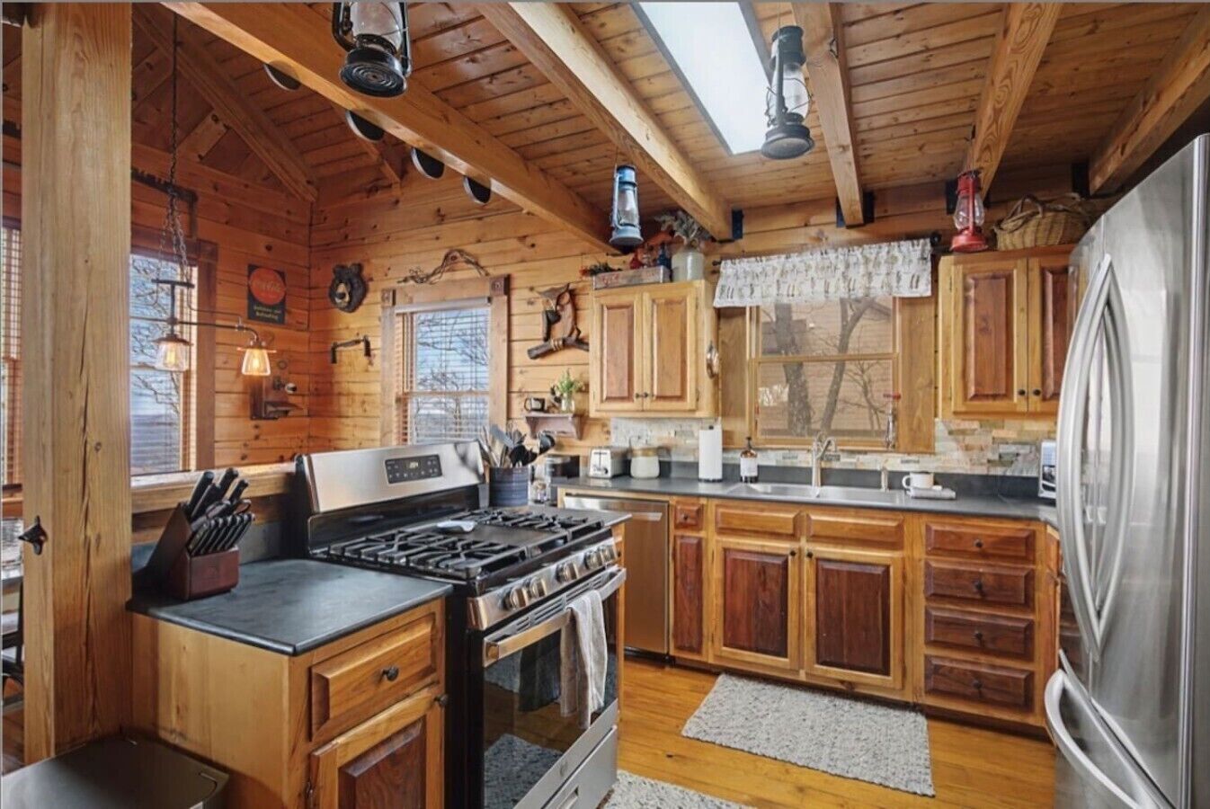 A wooden cabin interior with a kitchen featuring a stove, cabinets, and a refrigerator.