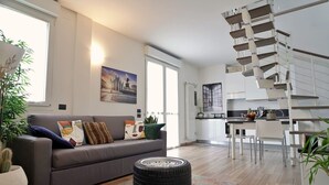A modern living room with a grey sofa, a small round table, and a spiral staircase leading to an upper floor. -  Rentopolis Apartments - Palazzo Candiani (Milan)