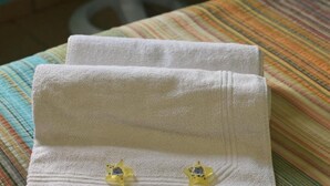 A neatly folded white towel with two yellow star-shaped earrings on it, placed on a striped fabric surface. - Double Room with Shared Bathroom (Leme Rio de Janeiro)