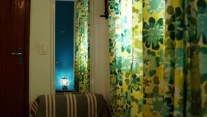 A room with a bed, a nightstand, a lamp, and curtains with a leaf pattern. - Double Room with Shared Bathroom (Leme Rio de Janeiro)