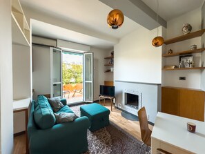 Een moderne woonkamer met een bank, poef, open haard en openslaande deuren naar een balkon.