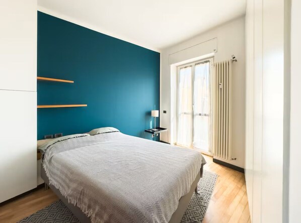 Een slaapkamer met een bed, nachtkastje, lamp en een raam met gordijnen.