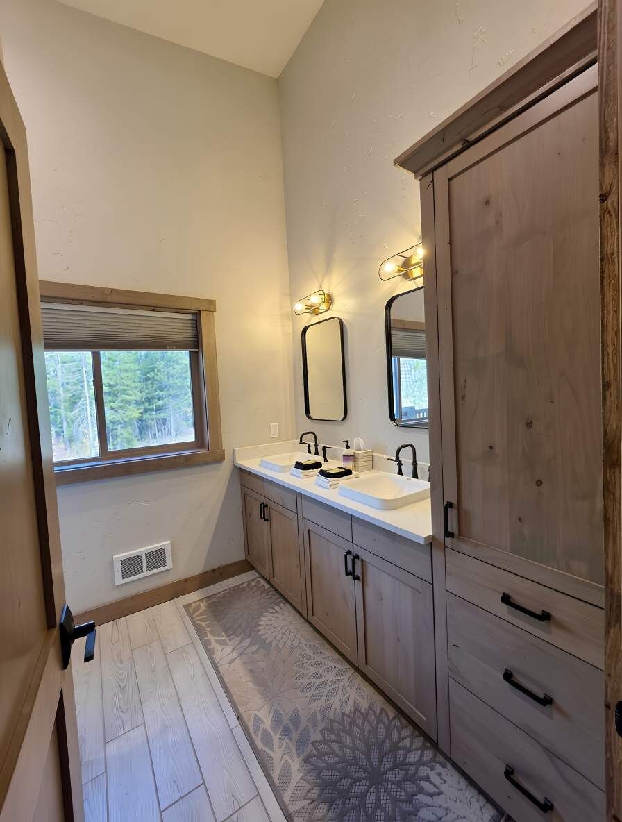 A bathroom with a window, two sinks, wooden cabinets, and a patterned rug.