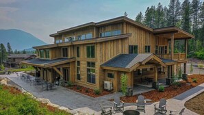Een modern houten huis met twee verdiepingen, voorzien van een patio met buitenmeubilair en een vuurkorf.