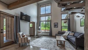 Een ruime woonkamer met een groot raam, een flatscreen-tv, een bank, een salontafel en een kamerkleed met dessin.