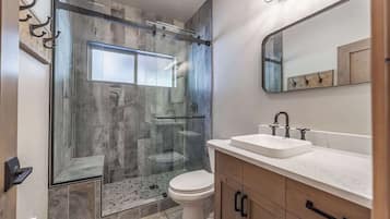 A modern bathroom with a glass-enclosed shower, a white toilet, and a vanity with a sink and mirror.