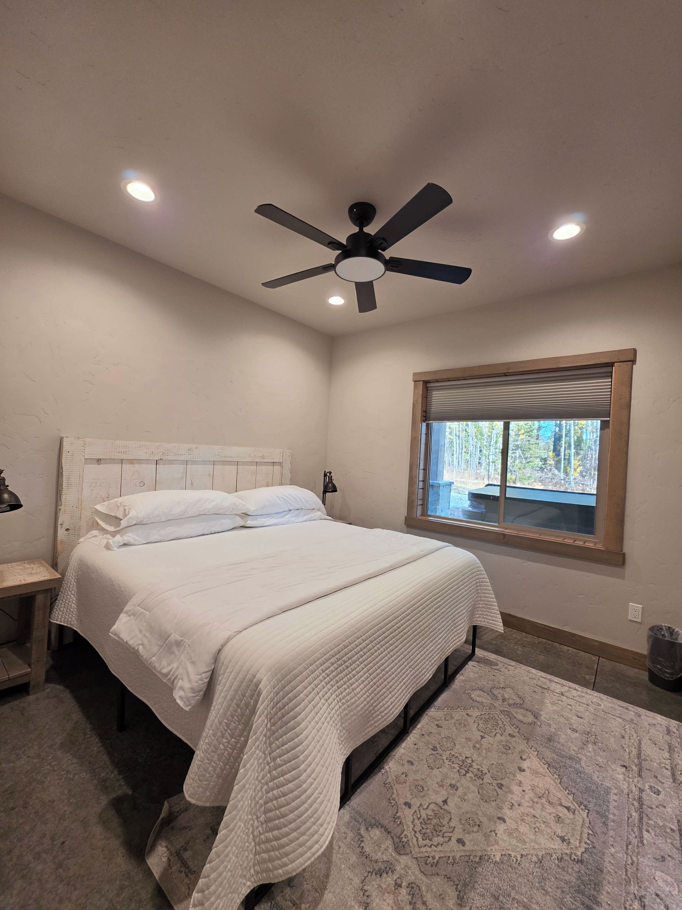 A bedroom with a bed, a ceiling fan, a window, and a nightstand.