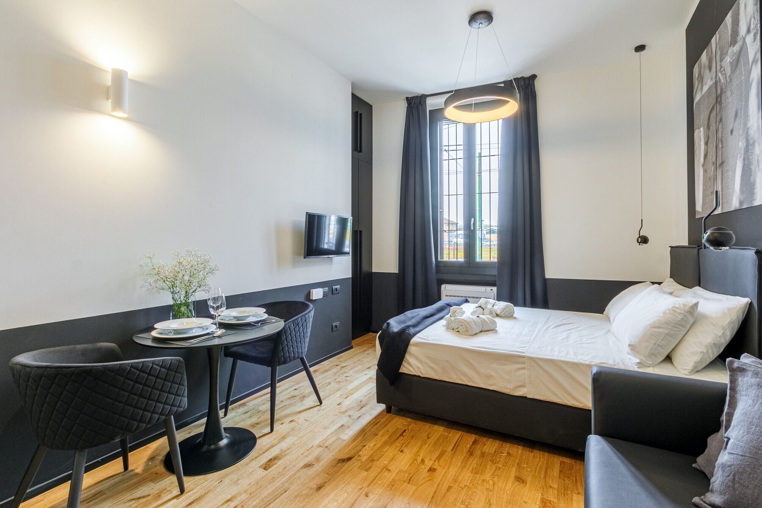 Una habitación de hotel moderna con una cama, un escritorio con silla, un televisor y una ventana con cortinas.
