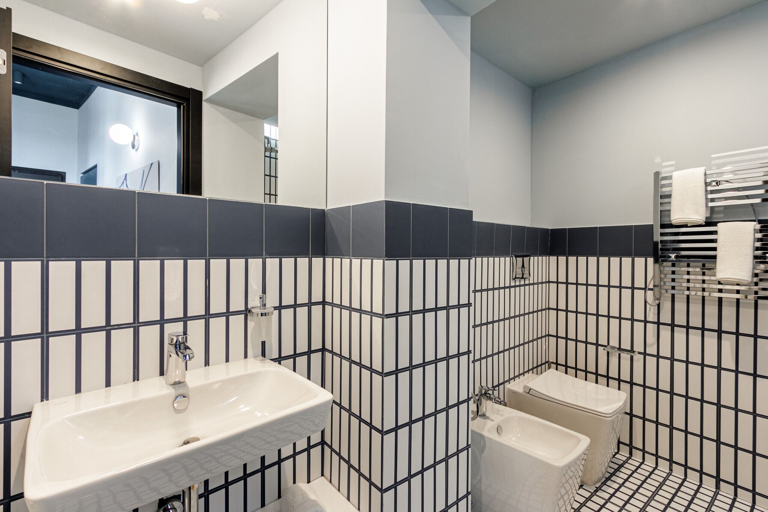 Une salle de bain moderne avec un lavabo blanc, deux toilettes et un miroir.