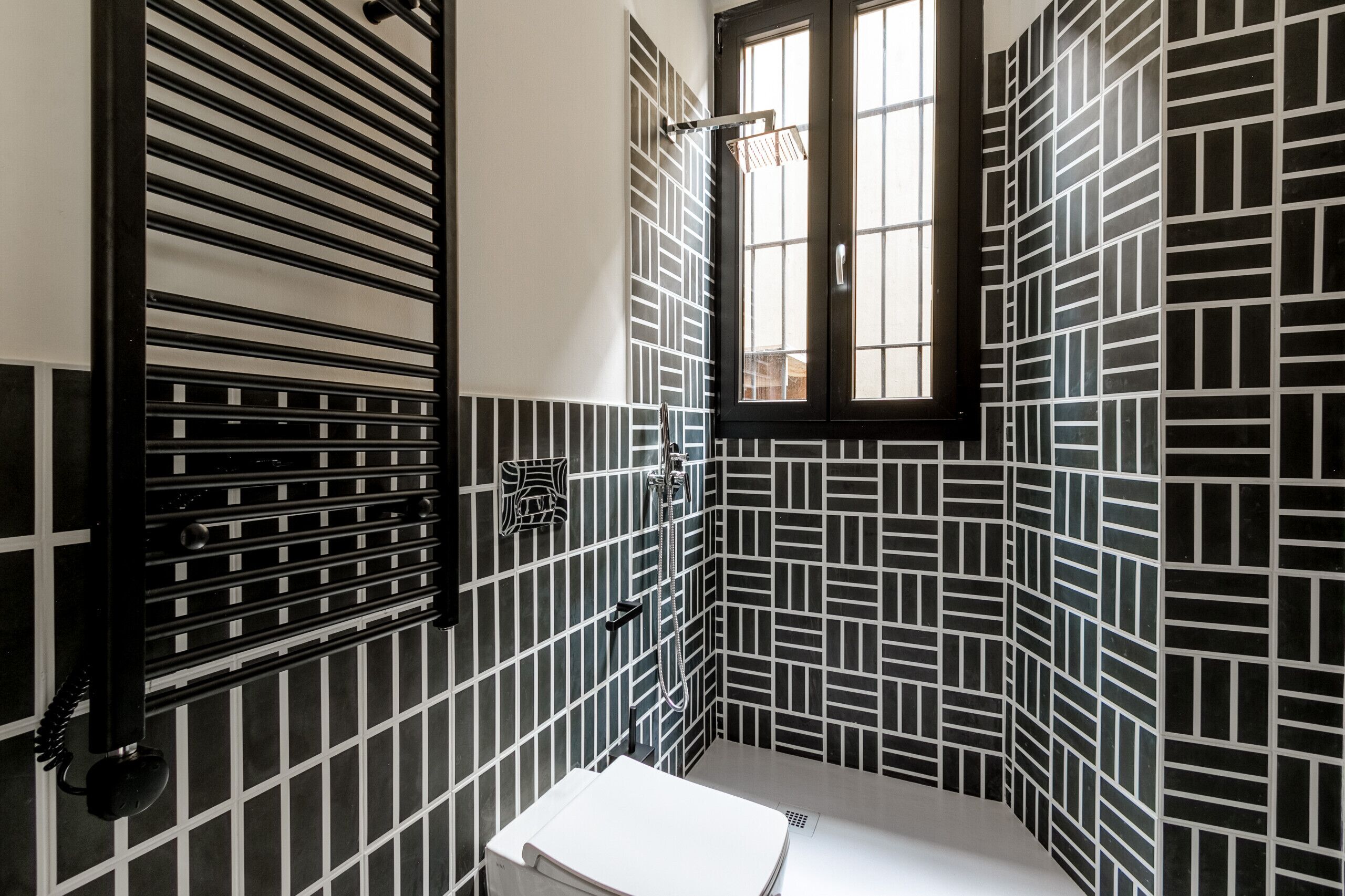 Un baño con baldosas blancas y negras, un inodoro blanco y una ventana con toallero.