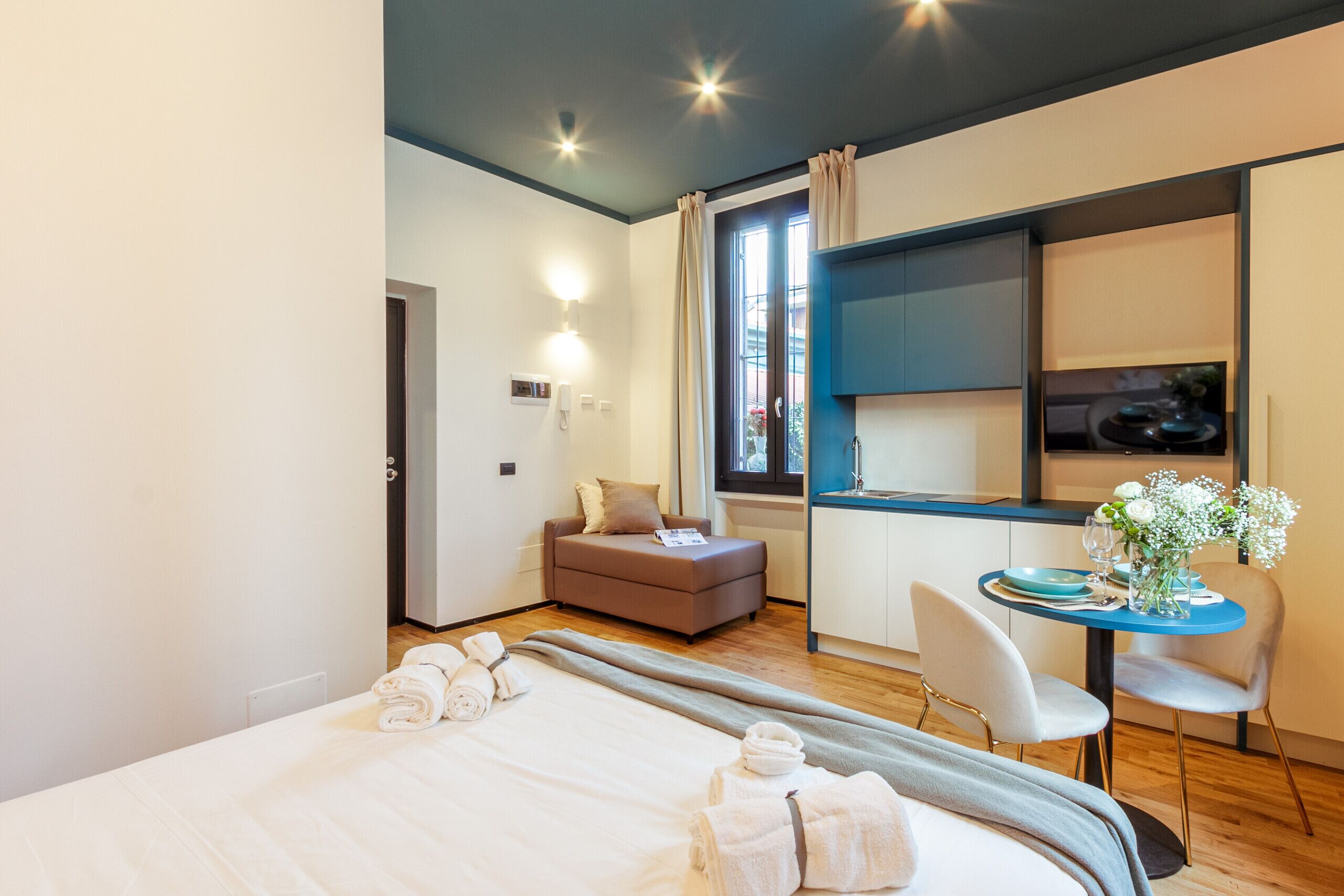 Een moderne hotelkamer met een bed, een kleine zithoek, een eethoek met tafel en stoelen, en een kitchenette.