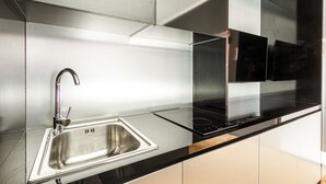 Une cuisine moderne dotée d’un évier en acier inoxydable, d’un plan de travail noir et d’une plaque de cuisson intégrée.