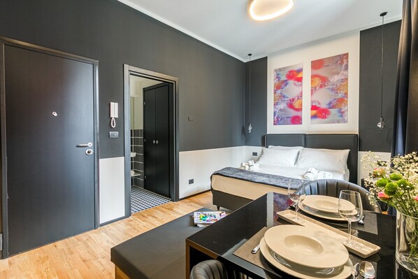 A modern hotel room with a bed, bedside table, and a dining area set for two.