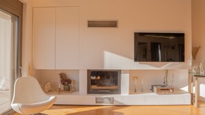 Ein modernes Wohnzimmer mit Kamin, Flachbildfernseher und einem weißen Sessel.