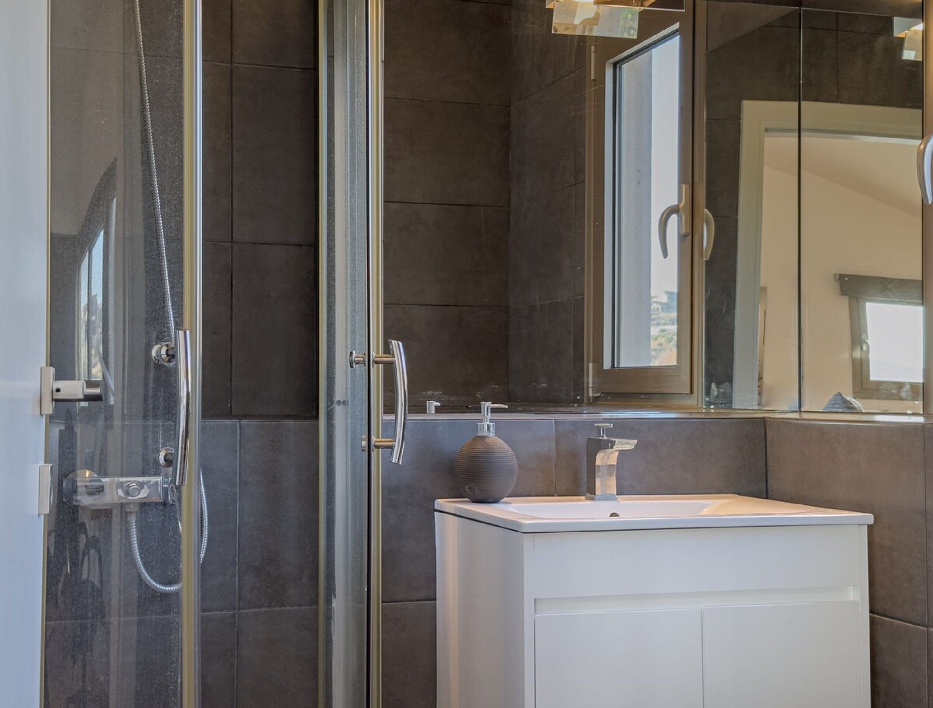 Une salle de bain moderne avec une douche à parois de verre, un lavabo blanc et un grand miroir.