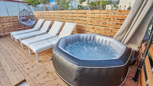 Un patio in legno con idromassaggio, poltrone relax e una sedia a dondolo.