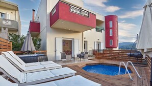 Area piscina sul tetto con poltrone relax, un solarium in legno e vista sugli edifici circostanti.