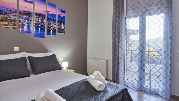 Una camera d'albergo con un letto, un comodino, una foto appesa al muro e una vista attraverso una finestra con tenda.