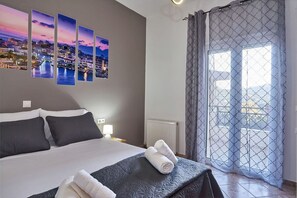 Hotelkamer met een bed, nachtkastje, een foto aan de muur en uitzicht door een raam met gordijn.