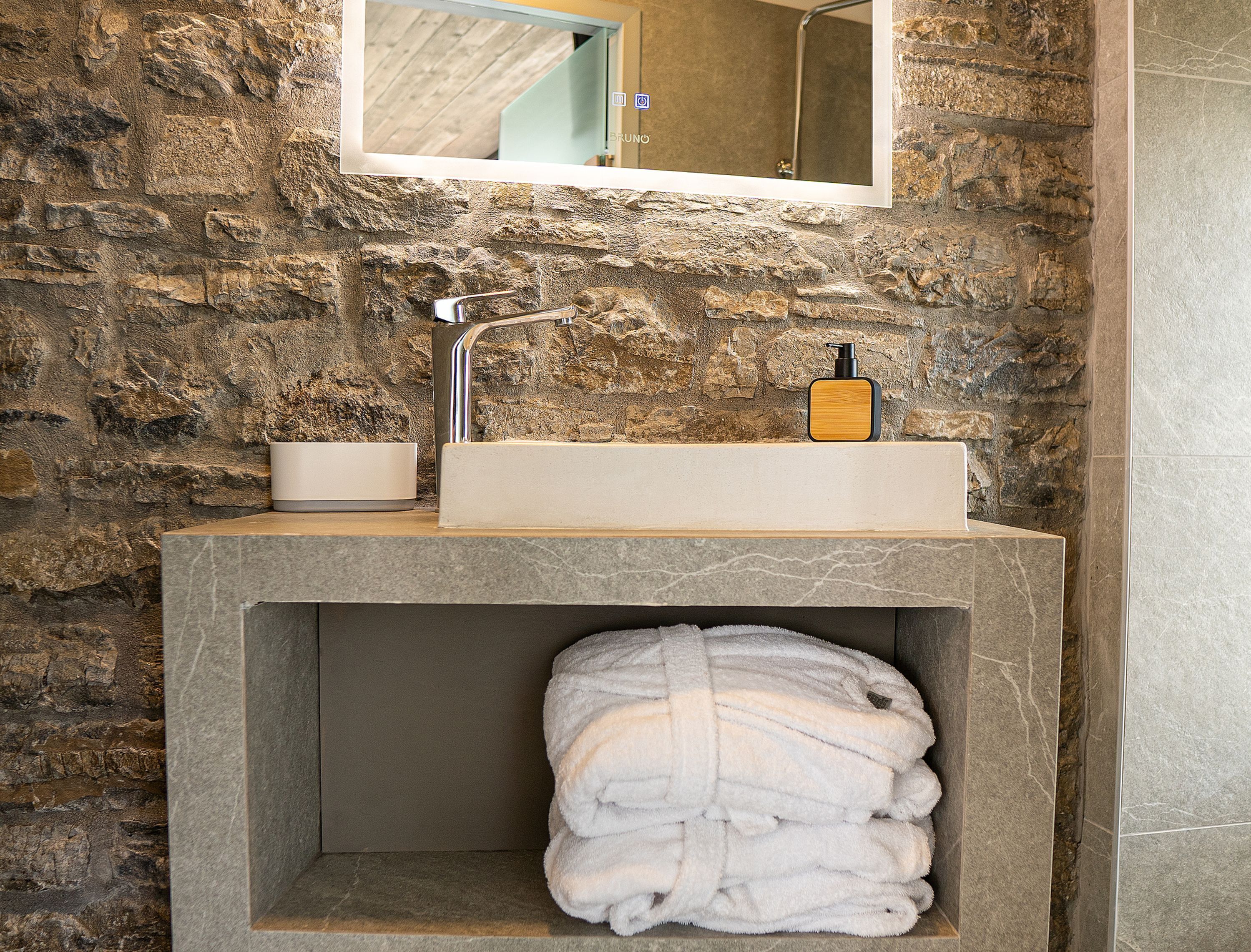 A bathroom with a stone wall, a rectangular sink, a mirror, and a towel rack.
