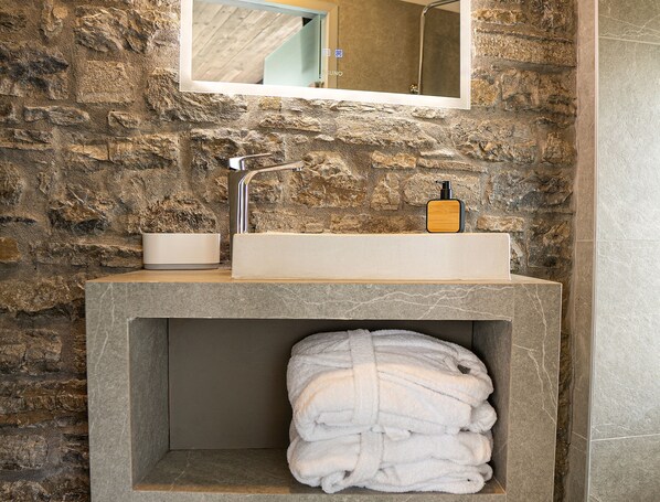 A bathroom with a stone wall, a rectangular sink, a mirror, and a towel rack.