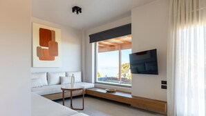 Una sala de estar moderna con un sofá blanco, una pequeña mesa redonda, un televisor de pantalla plana montado en la pared y un ventanal con vistas al exterior.