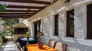 Une terrasse extérieure avec un mur en pierre, un barbecue et une table avec des chaises.
