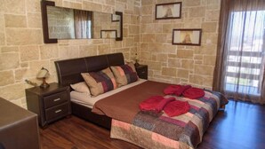 Une chambre avec un mur en pierre, un grand lit avec de nombreux oreillers, une table de chevet avec une lampe et des tableaux encadrés accrochés au mur.