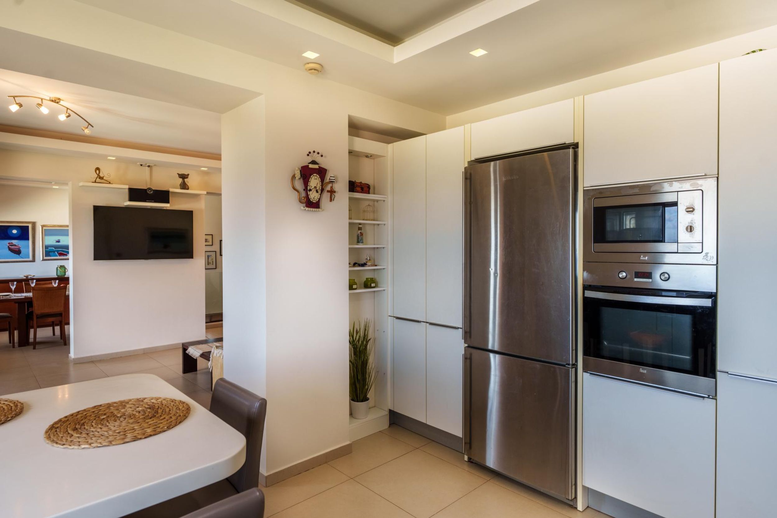 A modern kitchen with stainless steel appliances, white cabinetry, and a dining area with a white table and chairs.
