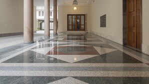 Un vaste hall d’entrée doté d’un sol en marbre à motifs géométriques, de grandes colonnes et d’une porte en bois située sur le côté droit.
