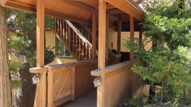 A wooden cabin with a covered porch, a staircase, and a view of the surrounding forest. - Little Slice of Heaven (Wofford Heights)