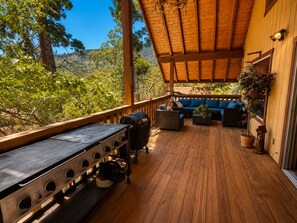 A covered outdoor deck with a grill, seating area, and a view of the surrounding forest. - Little Slice of Heaven (Wofford Heights)