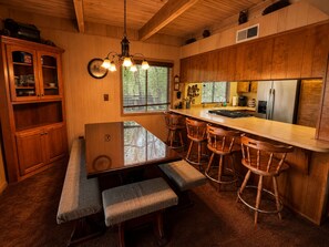 A wooden kitchen with a central island, bar stools, and a dining table with benches. - Little Slice of Heaven (Wofford Heights)