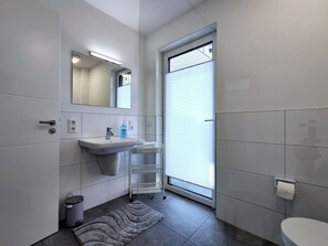 Et moderne badeværelse med vask, spejl, toilet og et vindue med persienner.