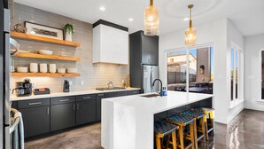 Une cuisine moderne dotée d’un îlot central, de tabourets de bar et de luminaires suspendus.