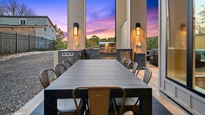 Un espace extérieur aménagé pour les repas, avec une longue table et des chaises, un barbecue et une vue sur le coucher du soleil.