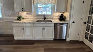 A kitchen with white cabinets, a marble countertop, a stainless steel dishwasher, and a window with a leaf-patterned valance. - Newly renovated home in Quiet Neighborhood. Great for Families (Dunn)
