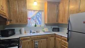 A kitchen with wooden cabinets, a stove, a microwave, a toaster, and a refrigerator. - Relaxing cabin in the woods. Unplug. Listen to the birds.  Smell the pines. (Pioneer)