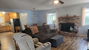 A living room with a sectional sofa, a fireplace, and a kitchen in the background. - Relaxing cabin in the woods. Unplug. Listen to the birds.  Smell the pines. (Pioneer)