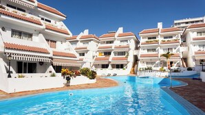 A swimming pool surrounded by white buildings with red-tiled roofs and balconies. - Home2Book Vibrant Las Américas Apt, Pool Retreat (Playa de la Américas)