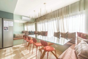 A dining area with a glass table, red chairs, a sofa, and a chandelier.