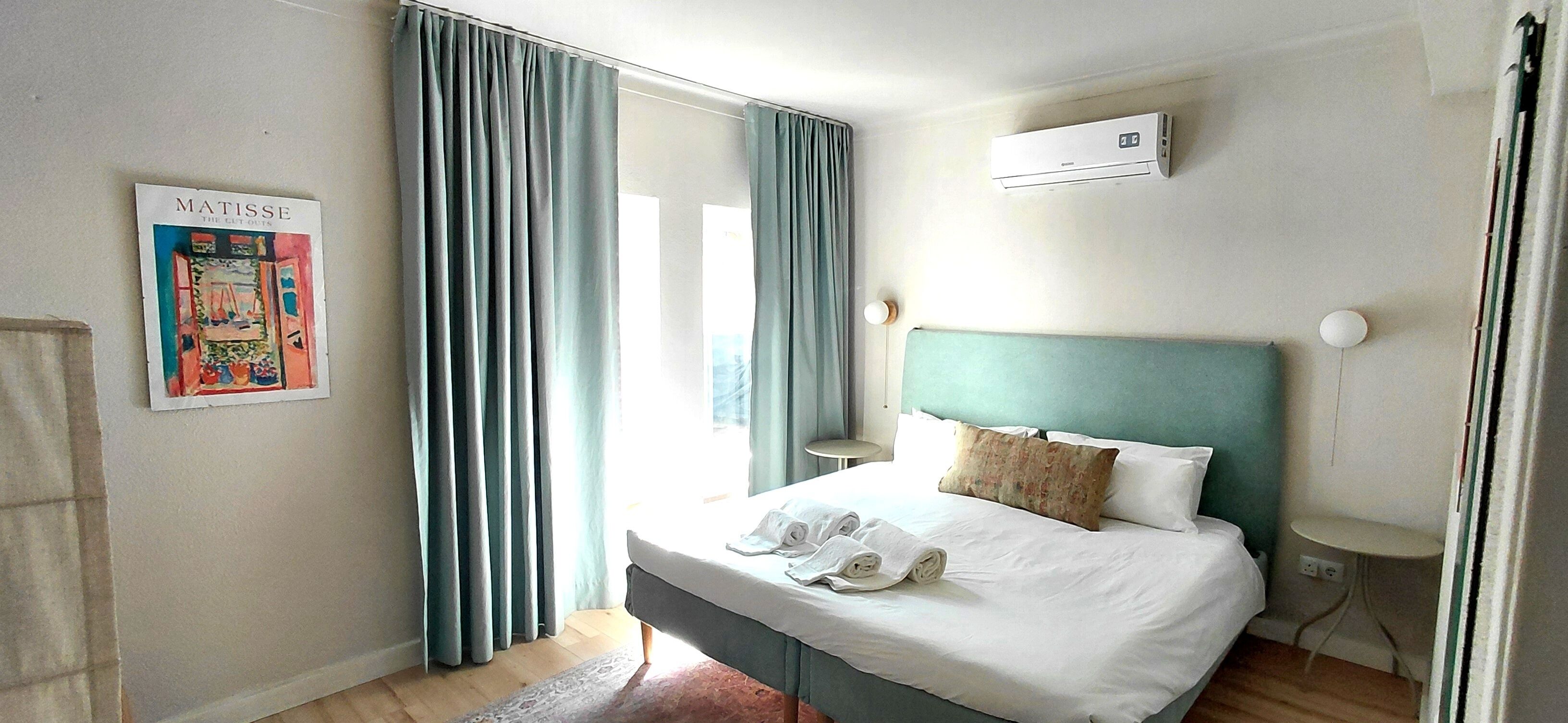 Ein Hotelzimmer mit einem Bett, einem Nachttisch, einer Wand-Klimaanlage und einem Poster an der Wand.