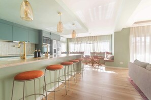 A modern kitchen with bar stools, a dining area with a table and chairs, and a living room with a sofa.